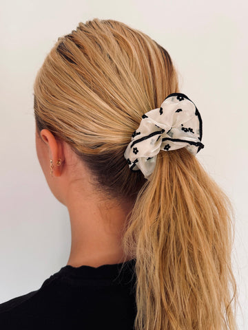Woman with blonde hair tied in a ponytail with a decorative scrunchie on a white background