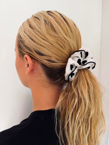 Person with blonde hair tied in a ponytail using a white scrunchie with black patterns against a white background